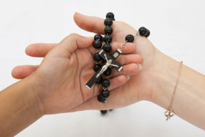 An adult and child hand together holding a rosary