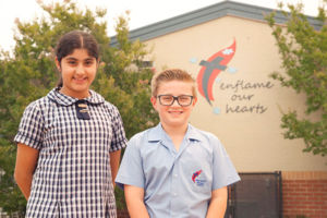 Two students smiling and standing in front the school motto "enflame our hearts"