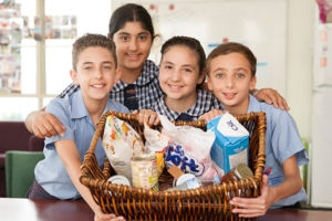 Four students smiling and showing a basket full of goods to give to charity