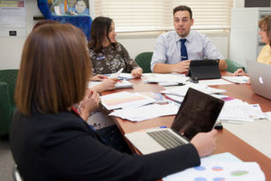 Staff members sitting at a table in discussion and using laptops and paper