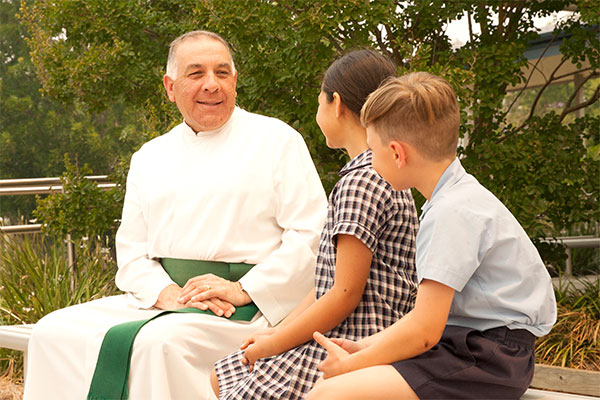 Principal Brother Nicholas of Holy Spirit Catholic Primary School sitting and chatting with two students